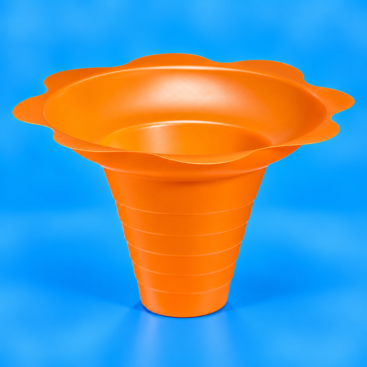 An orange plastic flower-shaped shaved ice cup or funnel with a flared rim and ribbed tapered base, shown on a solid blue background.