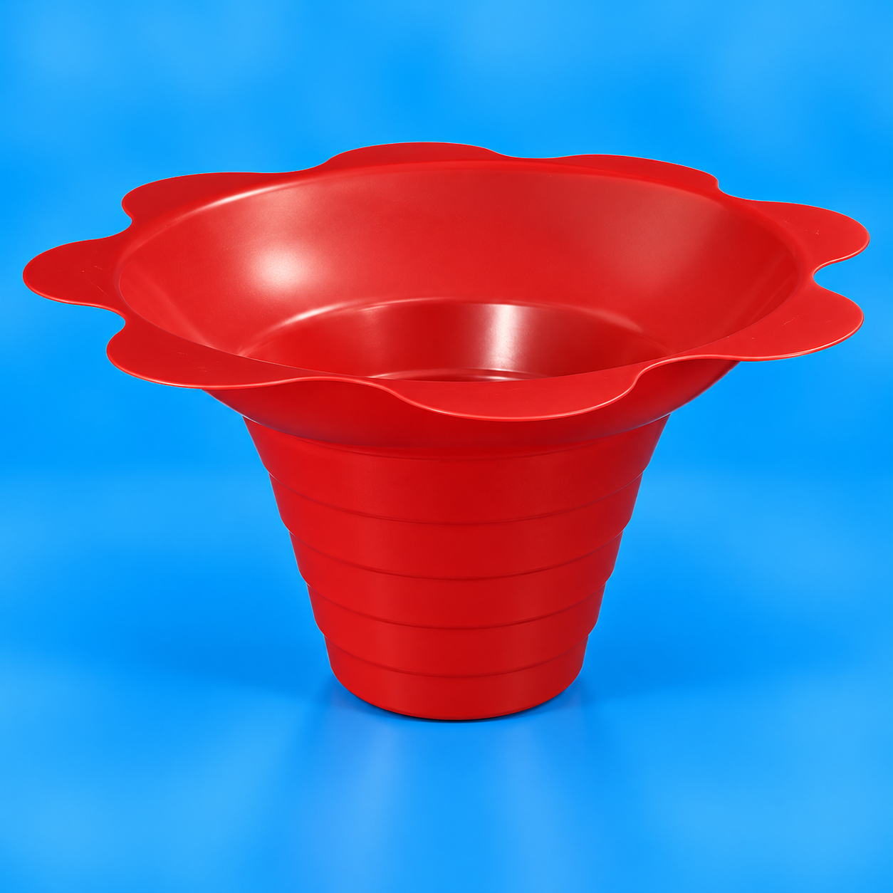 A bright red plastic shaved ice flower-shaped cup or bowl with a flared rim and ribbed tapered base, photographed on a smooth blue studio background.